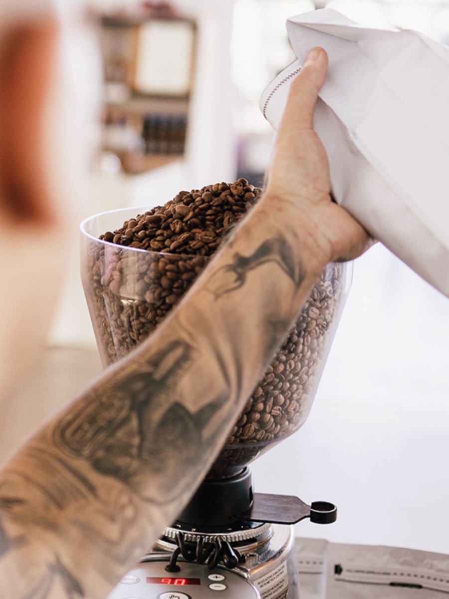 Fresh coffee beans being poured into a grinder hopper