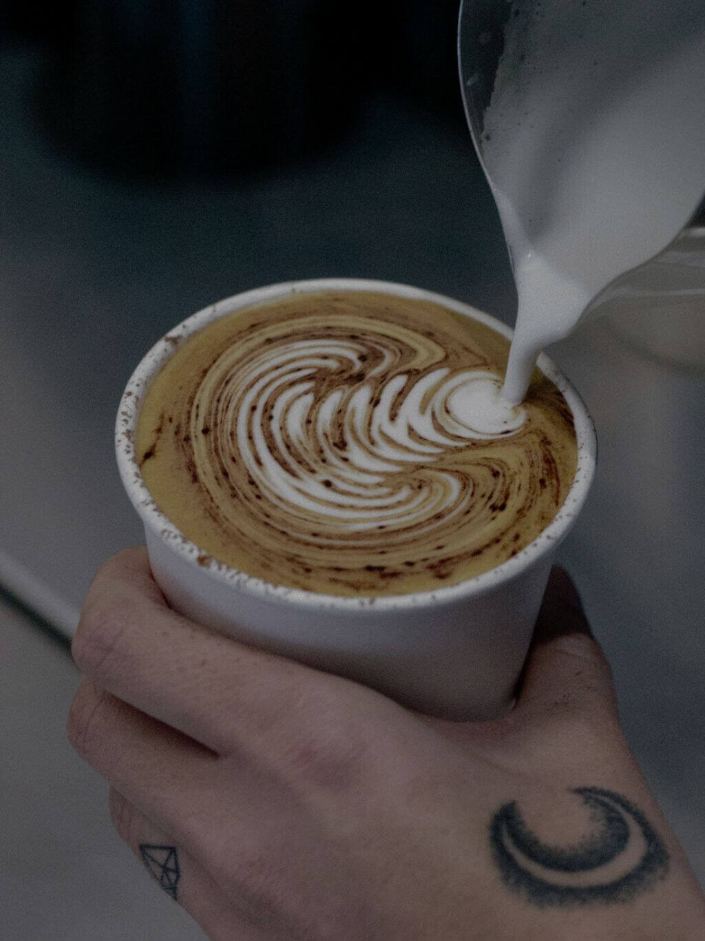Barista pouring milk creating latte art in a takeaway coffee cup