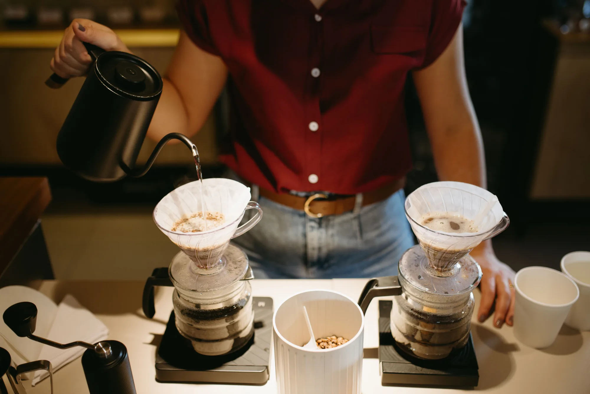 A barista pouring water over two V60-style pour-over drippers at a professional bar