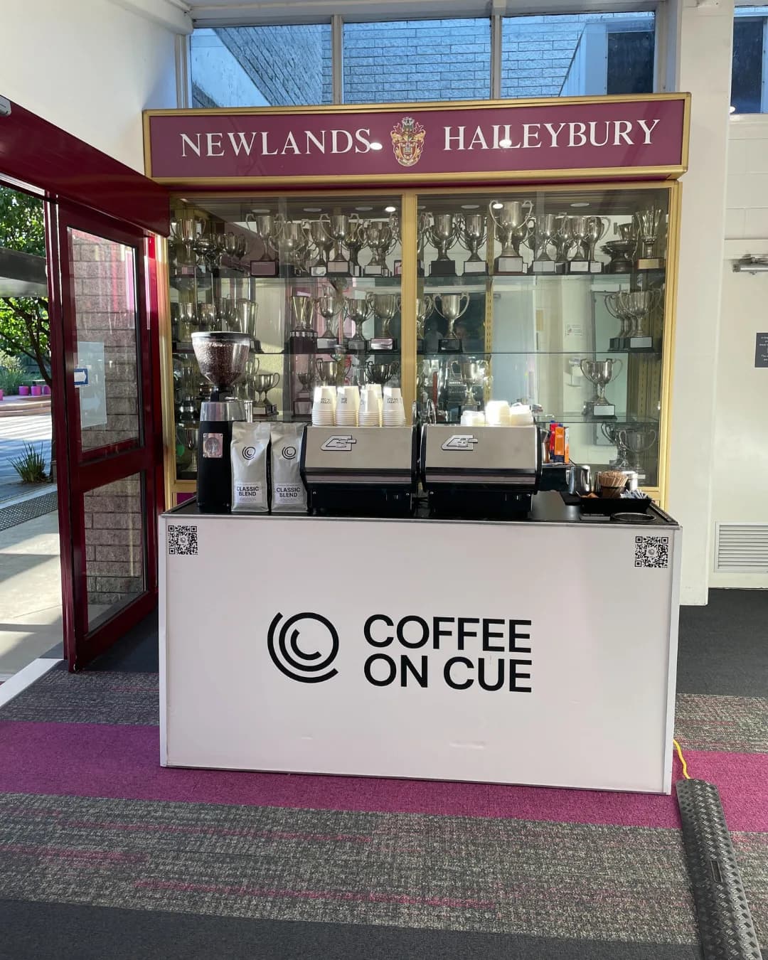 A branded Coffee on Cue cart in a school trophy cabinet foyer