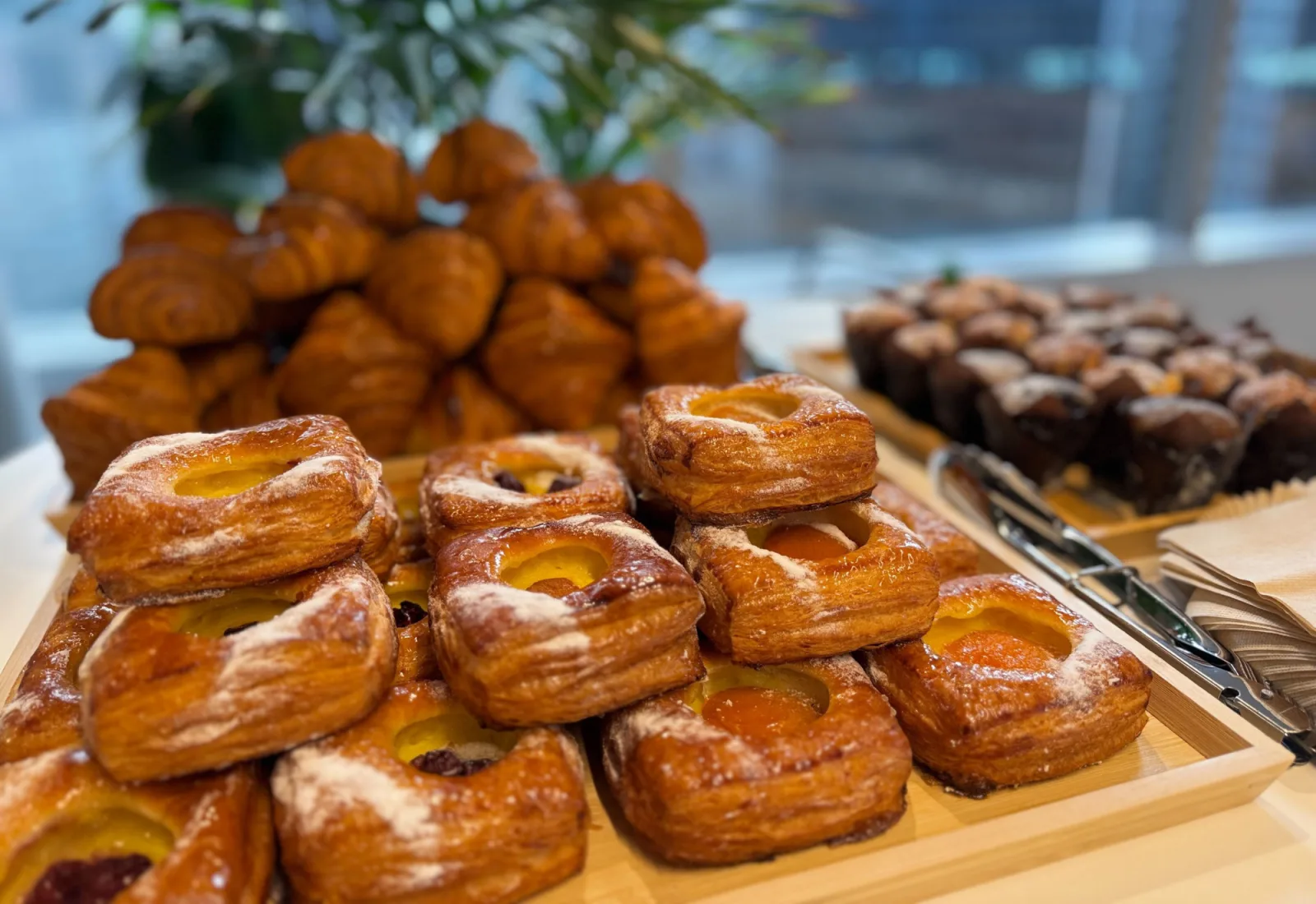 A catering spread of fresh danishes, croissants and brownies on wood trays at an event