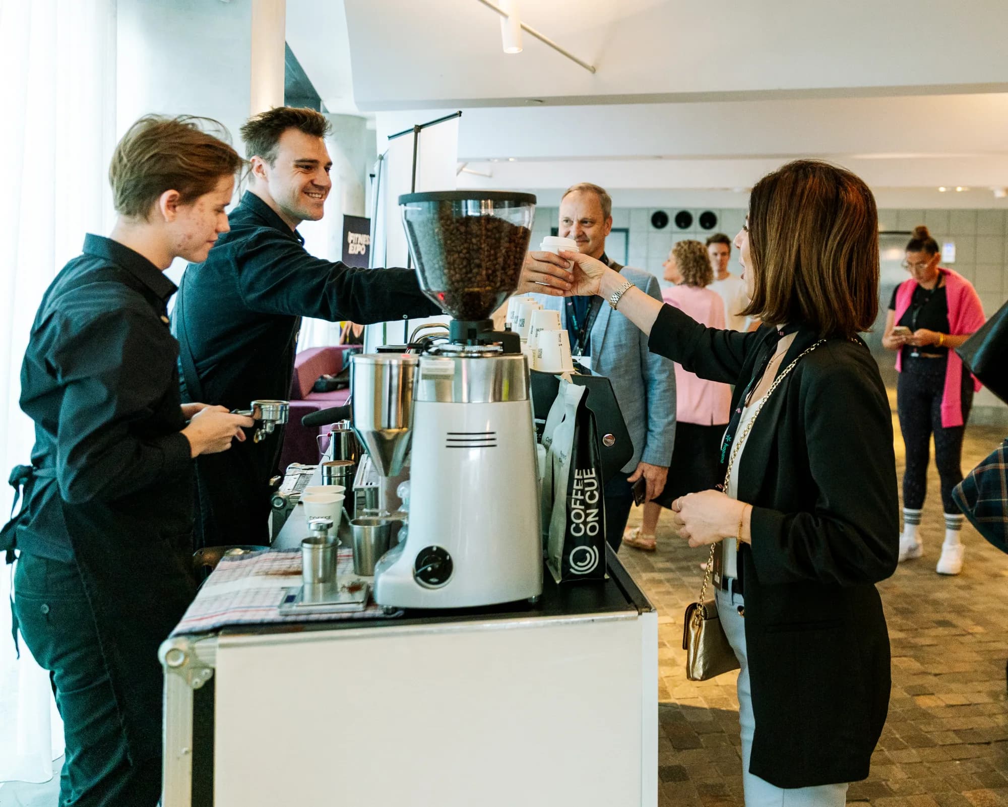 A Coffee on Cue barista handing a coffee to a guest at the machine