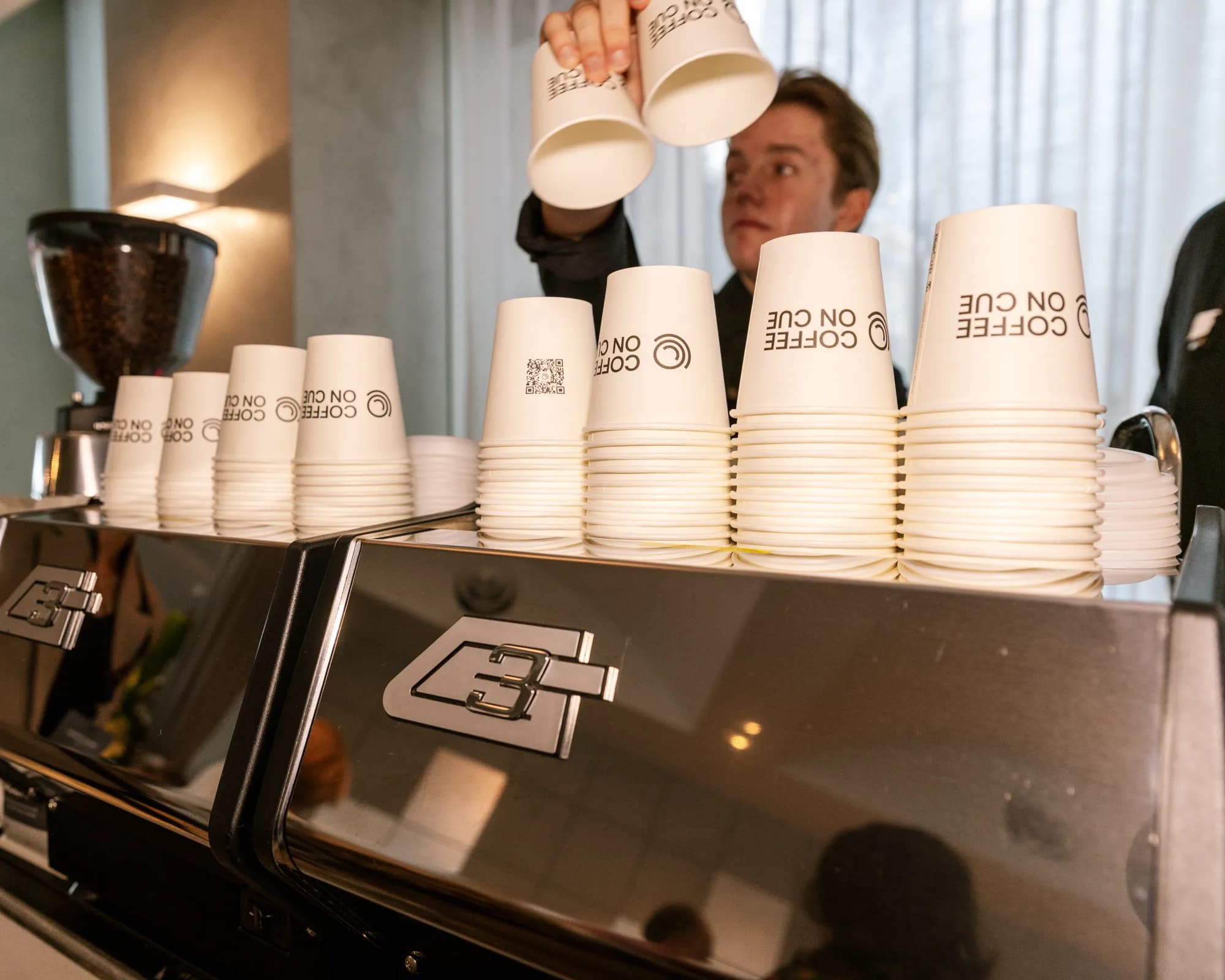 A Coffee on Cue barista handling stacked branded cups at the cart