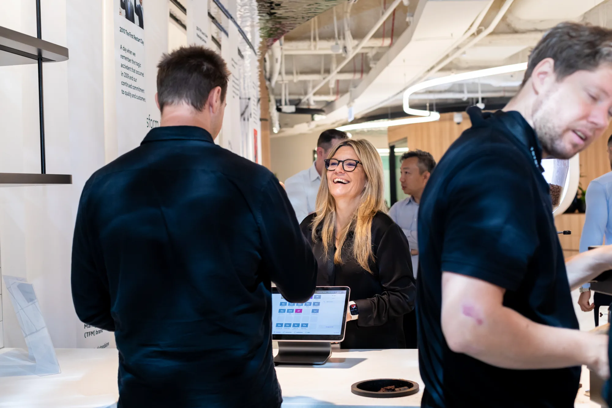 A colleague laughing with the barista across the Toyota Financial Services counter while ordering at the Coffee on Cue tablet