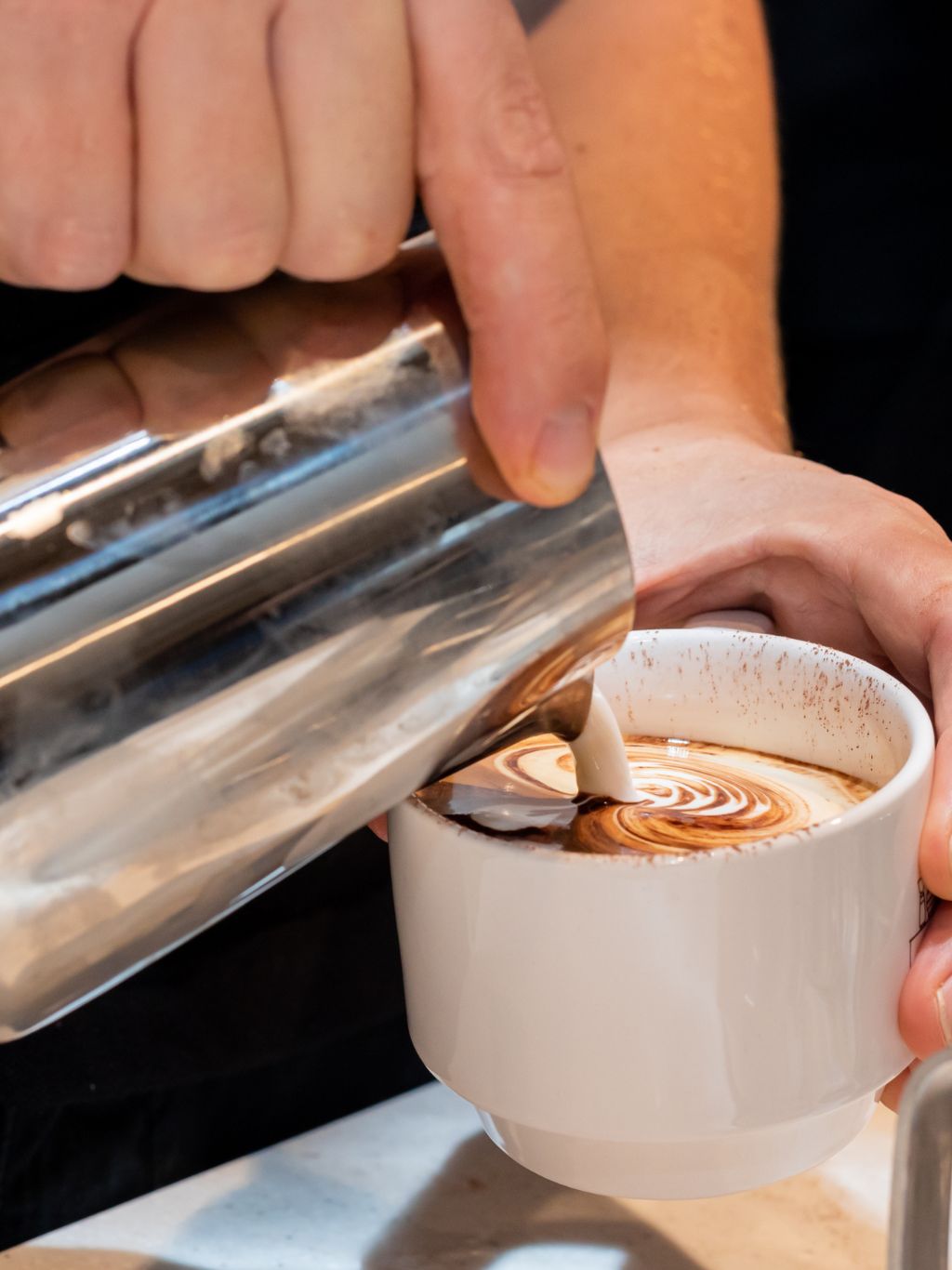 Workplace barista pouring coffee into ceramic mug