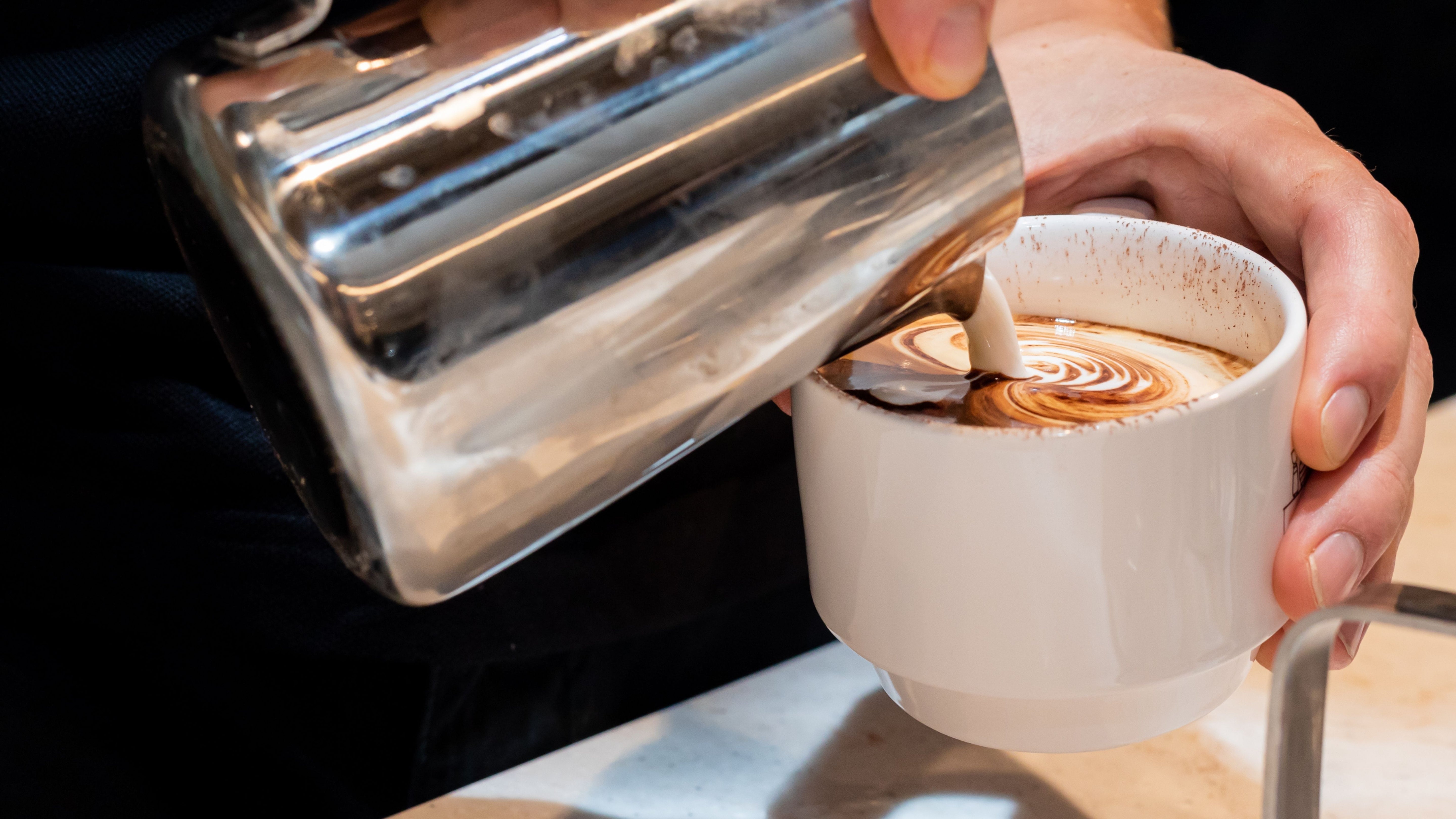 Workplace barista pouring coffee into coffee on cue ceramic cup