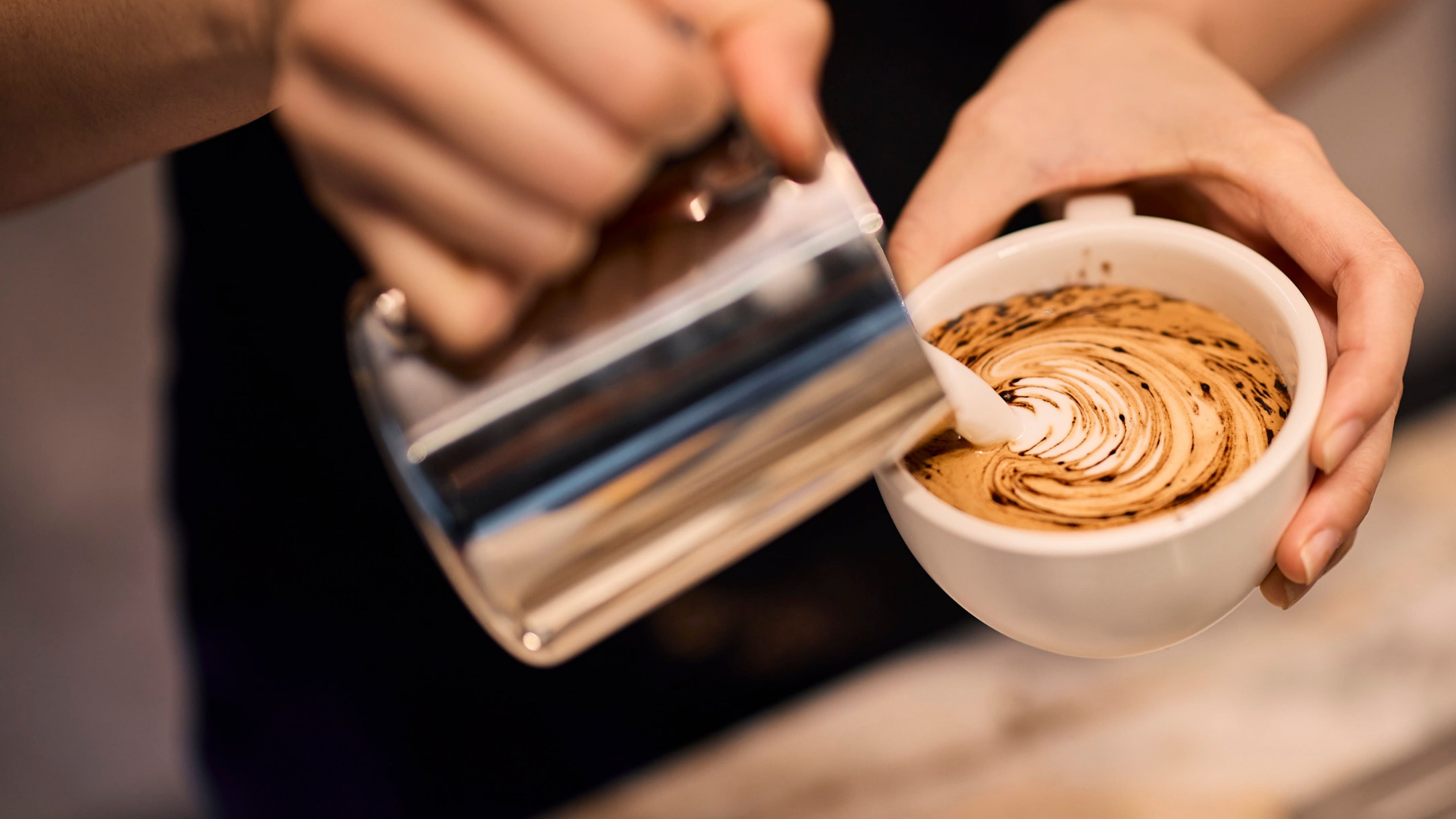 Barista pouring latte art into a ceramic mug